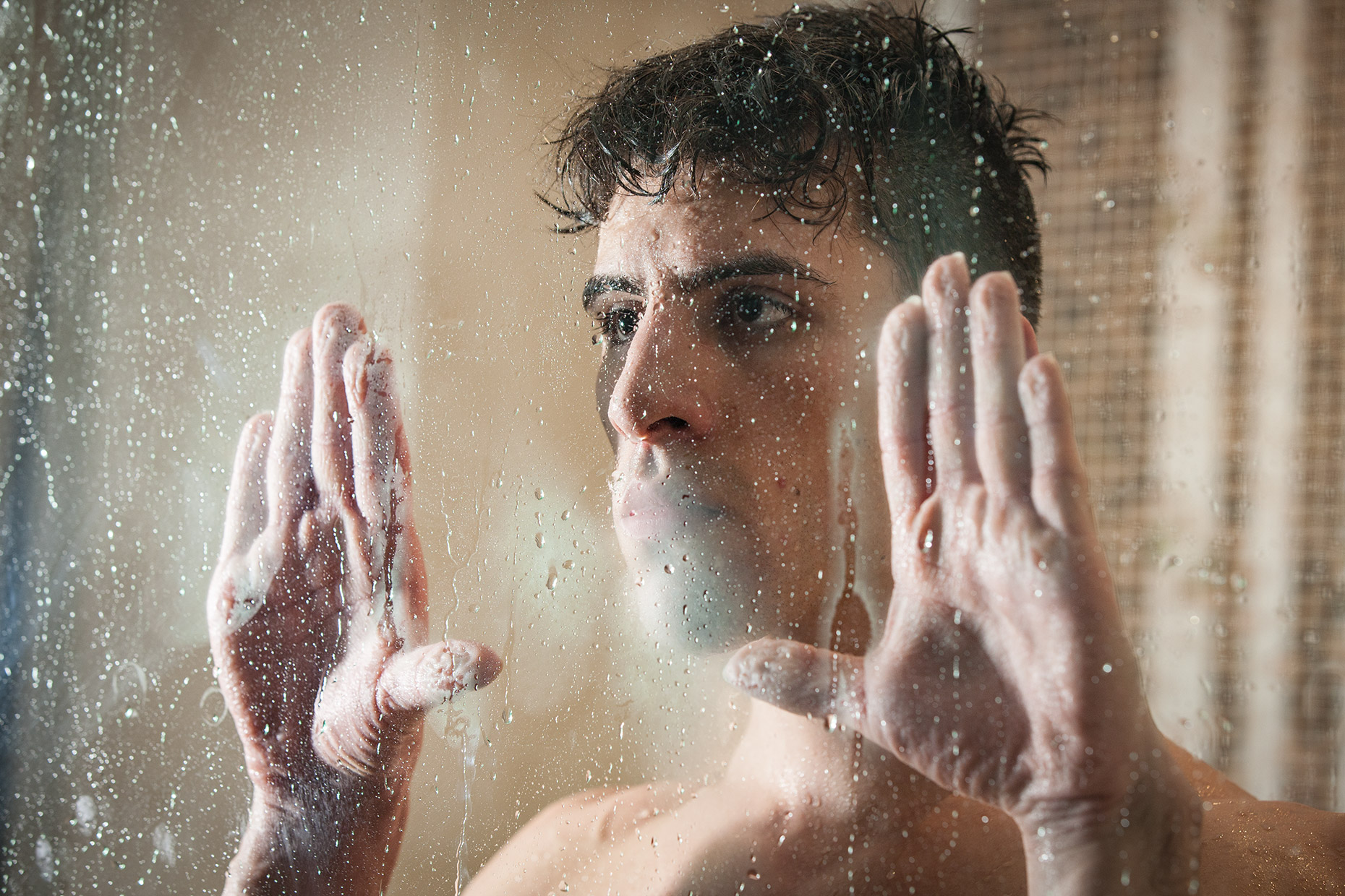 A man looking through a foggy glass window. Fine art editorial portrait.