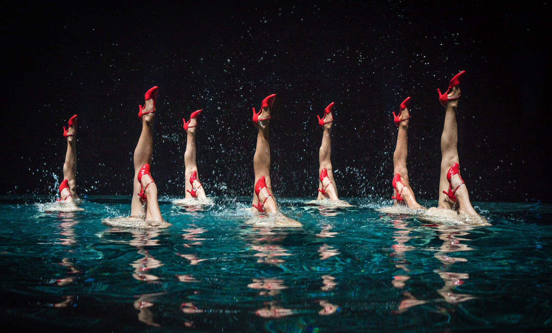 synchronized swimmers legs with red shoes coming out of the water with drops of water surrounding them. Advertising photo for the aquatic show Le Rêve at Wynn Las Vegas. Show . Cirque du Soleil.